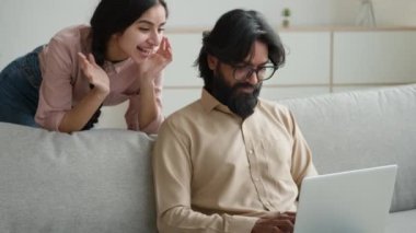 Kanepedeki Arap çift bilgisayar alışverişi yapıyor internetten internet alışverişi yapıyor çok ırklı koca heyecanlı müşteriler arıyor kadın ve erkek evdeki internet sitesinden mal satın alıyorlar