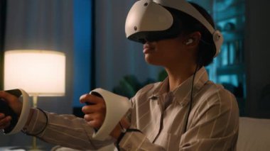 VR miğfer gözlüklü Afro-Amerikalı etnik kız video oyunu oynuyor sanal gerçekliği keşfediyor metaçağ gece siber uzayı yeni üç boyutlu dünya simülasyon gözlükleri ve evde gece eğlencesi düzenleyenler.