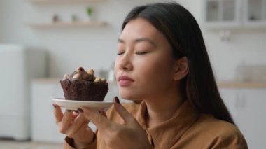 Aç Asyalı Koreli Japon kadın ev mutfağında tatlı pasta yemek istiyor sağlıksız yemek çikolatalı kek lezzetli fırın tatlı şeker bağımlılığı aşırı beslenme kilo kalorilerini muhafaza ediyor