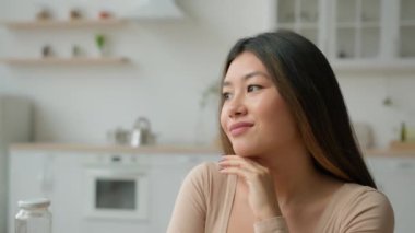 Asyalı hayalperest etnik kadın sakin kız Japon Çinli kadın ev hanımı ev sahibi kadın ev sahibi evde hayal kuruyor huzurlu bir şekilde yan tarafa bakıyor gelecek planları düşünüyor hayal gücü gülüşü hayal ediyor