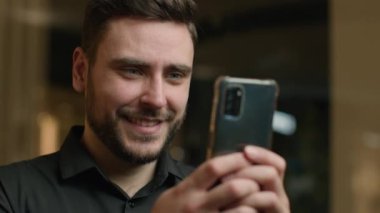 Kafkasyalı yetişkin işadamı cep telefonu medyası haberleri okuyor mutlu iş adamı, girişimci, işveren erkek ofis müdürü akıllı telefon e-posta mesajları gülüşünü içeride tarıyor.