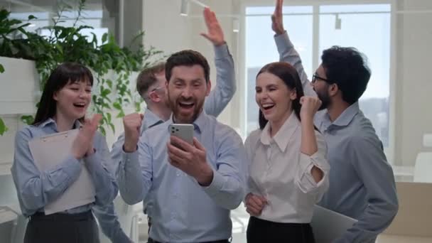 成功したグループビジネスの人々 多国籍多国籍オフィス チームの同僚 幸せな興奮したビジネスマンのビジネスマン ビジネスマンは 携帯電話で良いニュースを読む 勝利の商業オファーを祝います オンライン賭け — ストック動画