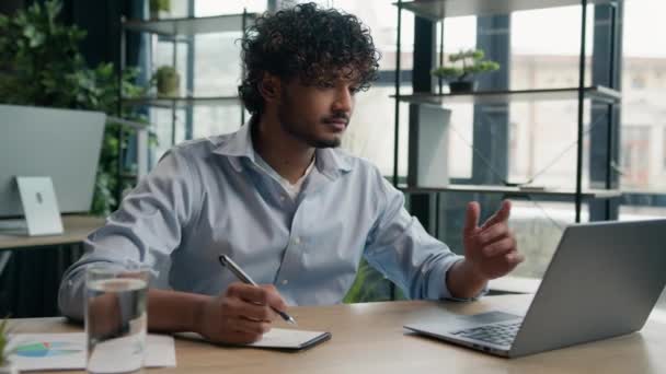 アラビアのインドのラテン語の男のビジネスマンはノートブックでビジネスノートのアイデアを書きます 会社のタスクを管理する 机の上のペンでスケジュールを書く オフィスのラップトップコンピュータで働く男性労働者の従業員 — ストック動画