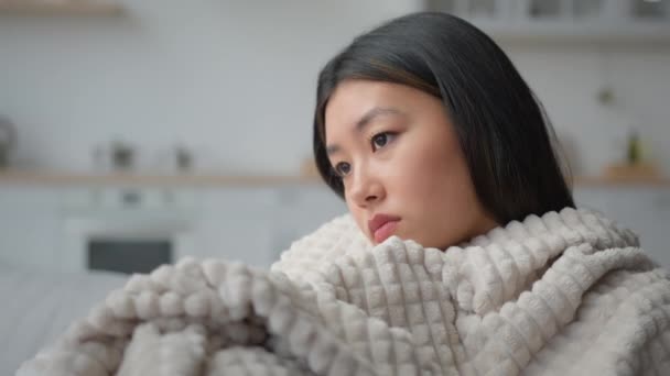 闷闷不乐闷闷闷不乐的亚洲女人独自在家裹着毛毯思考问题的日本女人陷入沉思的女孩在公寓里忍受着寒冷的心理问题焦虑忧郁症悲痛困扰 — 图库视频影像