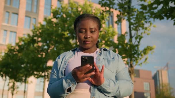 ハッピーアフリカ系アメリカ人女性学生ガールアウトドア 大学の近くで携帯電話をブラウジングの勝利成功スマートフォン勝利成功笑顔で叫ぶスマートフォン勝利成功成功は勝利興奮運を達成します — ストック動画
