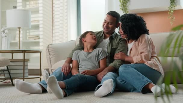 幸せな多人種家族 アフリカ系アメリカ人の両親は カフカシアの小さな息子と抱擁する 家庭のフロアトークで子供を養子に笑う 楽しい週末 笑顔の父親の母親と親指を示すかわいい子供 ジェスチャー — ストック動画