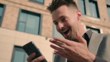 Şaşırtıcı mutlu iş adamı, cep telefonundan iyi haberler okuyarak SMS mesajı alıyor. Mutlu, başarılı, beyaz adam kazananı akıllı telefondan online zafere seviniyor.