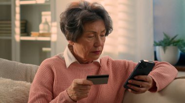 Kafkasyalı yaşlı kadın yaşlı yaşlı yaşlı yaşlı kadın olgun kadın emekli büyükannesi cep telefonu ve banka kredi kartıyla online alışveriş yapıyor akıllı telefonuyla evden internet ödemeli cep telefonu alıyor.