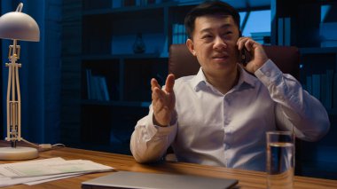 Mutlu Asyalı işçi yönetici yönetici yönetici yönetici girişimci gece ofisinde cep telefonuyla konuşuyor. Koreli iş adamı Çinli şirket CEO 'su Japon yatırımcı akşam geç saatlerde akıllı telefon konuşması yaptı