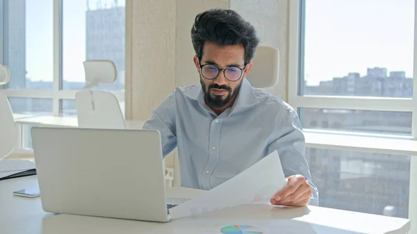 アラビア系インド人男性ムスリム男性実業家専門家経営者オフィスでラップトップで作業労働者マネージャー情報財務グラフは 紙のビジネス文書を読む — ストック写真