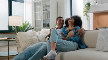 Gülen, kaygısız, Afro-Amerikan mutlu aile çifti evli, kadın, erkek, erkek, kız arkadaş, aile içi flört muhabbetleri gülüyor, kanepede aşk muhabbeti yapıyor.