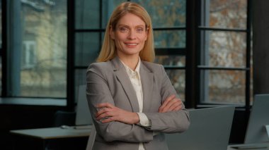 Smiling confident Caucasian middle-aged woman standing at modern creative office. Adult 40s businesswoman project manager lady executive business leader looking at camera arms crossed smile, portrait