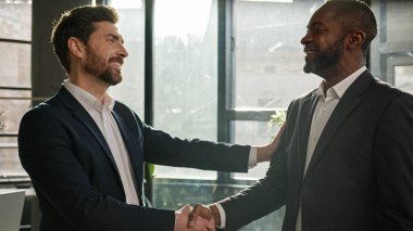 Caucasian boss hr manager man shake hand of African American candidate partner client making deal hiring thanking for collaboration congratulation. Diverse business partners men in office handshaking