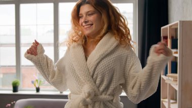 Hareketli kadın bacakları yatağa atlıyor Kafkasyalı mutlu kadın kaygısız ev sahibi kadın bornoz içinde yatak odasında zıplarken eğleniyor hafta sonu otel tatilinde eğleniyor.