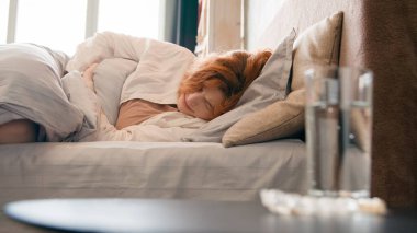 Bir bardak su ve ilaç tableti. Hasta, sağlıksız, yatakta acı çeken bir kız. Karın ağrısı, karın ağrısı, karın ağrısı.