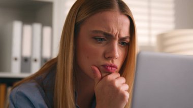 Ciddi kız kaşlarını çattı. Kafası karışmış beyaz bir kadın, bilgisayar monitörü, iş kazası, kötü haber. Düşünceli, düşünceli, düşünceli, web sorunu çözen bir iş kadını.