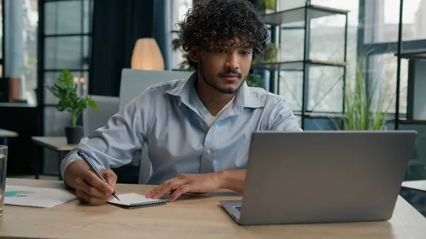 アラビアのインドのラテン語の男のビジネスマンはノートブックでビジネスノートのアイデアを書きます 会社のタスクを管理する 机の上のペンでスケジュールを書く オフィスのラップトップコンピュータで働く男性労働者の従業員 — ストック写真