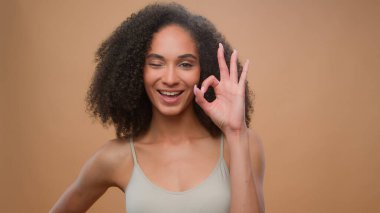 Afro-Amerikan model güzel çekici bir kız bej stüdyo arka plan güzellik prosedürü kameraya gülümsüyor tamam kabul et kozmetik reklamı sağlık cilt bakımı