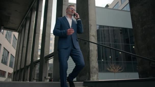 古い成熟したコーカサスビジネスマンに行くアウトドア 雇用主話スマートフォンは オフィス会社の近くの都市で話す携帯電話の散歩を交渉し 話す携帯電話のシニアビジネスマン — ストック動画