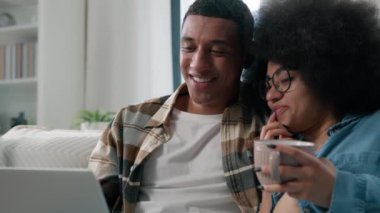 Afro-Amerikan mutlu aile çifti, erkek arkadaş, erkek arkadaş, kadın koca, bir fincan çay ve kahve. Evde dizüstü bilgisayar alışverişi yapan bir dükkanda bilgisayar başında film seyrediyor.