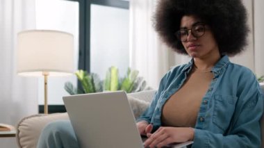 Kanepe üzerinde dizüstü bilgisayarla çalışan serbest çalışan, bilgisayarlı kadın kullanıcı ile meşgul olan Afro-Amerikalı bir kadın ev işi konuşmalarında bilgisayarla çalışan e-öğrenici kız.