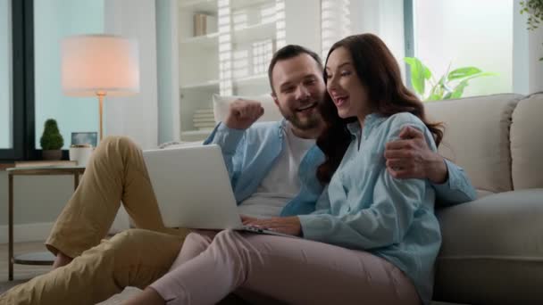 快乐的赢家白种人夫妇兴奋地在家里用笔记本电脑赢了成功的男人女人家庭在客厅里用电脑赢了在线上的胜利 — 图库视频影像