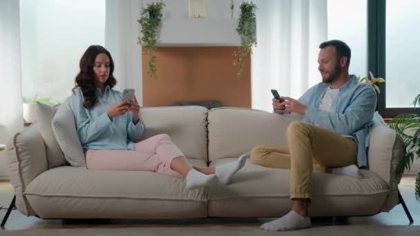 コーカサスガジェット中毒カップルは ソーシャルメディアスマートフォンゲームをスクロールする携帯電話で忙しく お互いのインターネット中毒を無視して 家庭のソファーの家族の男の女性の携帯電話中毒 — ストック動画