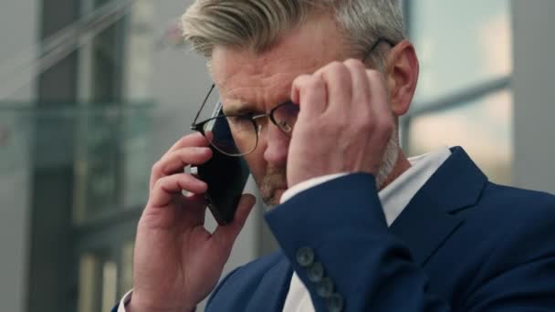 白种人退休的商人成熟的资深商人领导雇主谈论手机戴上眼镜结束电话把电话放在正式的夹克口袋里从长椅上站起来 — 图库视频影像
