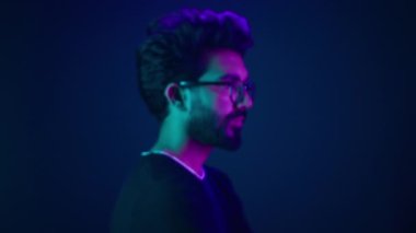 Neon ultraviyole mavisi arka plandaki erkek portresini kapat. Müslüman Arap profilde poz veriyor. Başını çevirip kameraya bakıyor.