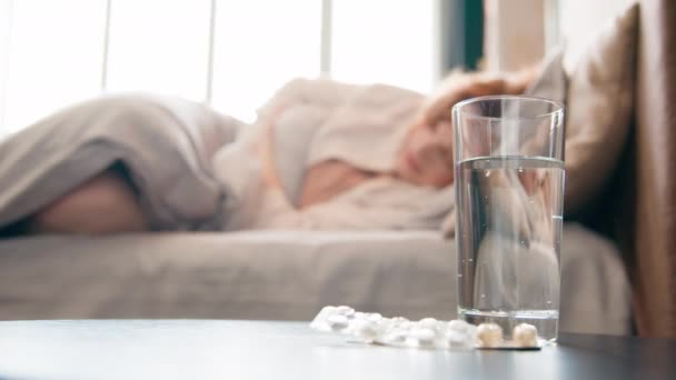 水のガラスと錠剤薬 テーブルの錠剤治療 不健康な不健康な女の子 寝室で苦しんでいるベッドで苦しんでいます 女性は胃痛の月経周期を感じます 痛みを伴う腹部 — ストック動画