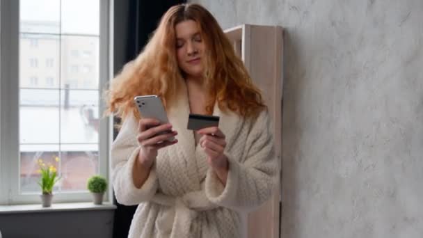 白种人快乐快乐的女人穿着浴衣在家里宾馆房间里早上的女店员客户用智能手机在线购物跳舞听音乐听歌曲用手机和信用卡购物 — 图库视频影像