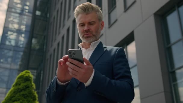 成熟的高级雇主白种人中年创业者户外运动的老商人看着手机思考沉思沉思的想法解决方案认为城市男性商人在浏览智能手机 — 图库视频影像