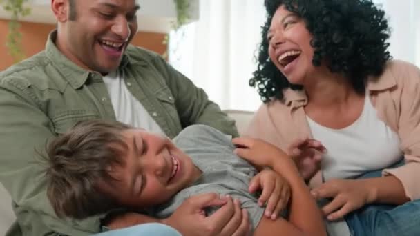 ハッピーマルチエスニック家族の母親とかわいい小さな男の子の息子は一緒にソファで楽しんでくつろいでいます ケアフリー アフリカ系アメリカ人の両親の子供は家で笑って遊ぶ ソファーで面白いゲームを楽しむ — ストック動画