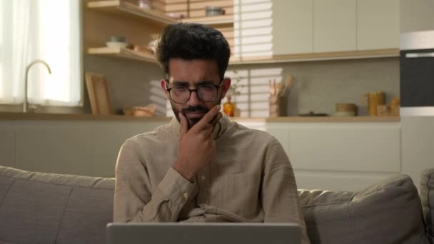 印度阿拉伯穆斯林男子在厨房里自由职业者商人在家里操作笔记本电脑困惑地耸了耸肩不知道男性客户困惑不确定怀疑怀疑不确定没有线索无助的损失 — 图库视频影像