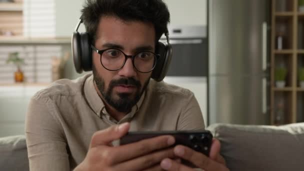 Chocado Desapontado Árabe Homem Fones Ouvido Segurar Telefone Celular Casa — Vídeo de Stock