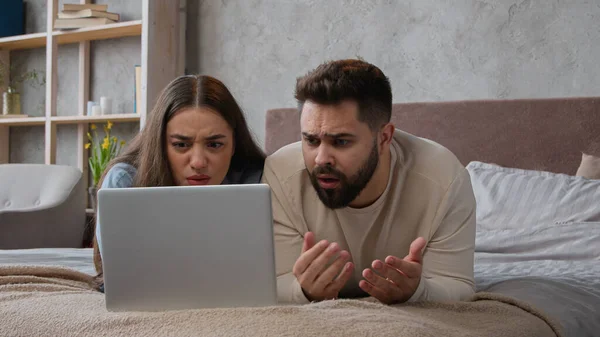 Desperate stressful Caucasian sad couple homeowners confused family wife husband read bad email trouble lost bank mortgage negative result computer failure anxious man and woman lying on bed at home