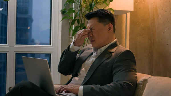 Sick Asian chinese korean male businessman tired exhausted man overworked late job with laptop in evening office downtown middle-aged entrepreneur suffer eyestrain eyes pain ache bad eyesight vision