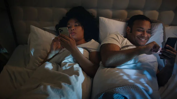 African American couple family man woman girlfriend boyfriend wife husband in dark bed home bedroom at night scrolling smartphones browsing mobile phones social media gadgets addict internet addiction
