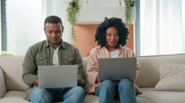 Afro-Amerikan aile çifti iki çok ırklı serbest çalışan kadın ve adam evlerinde dizüstü bilgisayar kullanarak çalışıyor uzaktan alışveriş yapan internet araçları birbirlerine bakıp gülümsüyorlar.
