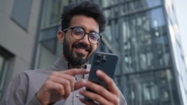 Mutlu Hintli Arap işadamı cep telefonu aygıtını açık havada kullanıyor. Harika bir erkek işveren buluyor. Şanslı kazanan online bahis başarısını kazanıyor.