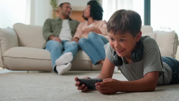 非裔美国人父母母亲父亲坐在沙发上聊天小男孩在地板上玩网络游戏手机上网成瘾智能手机快乐的多种族家庭在家里休息 — 图库视频影像