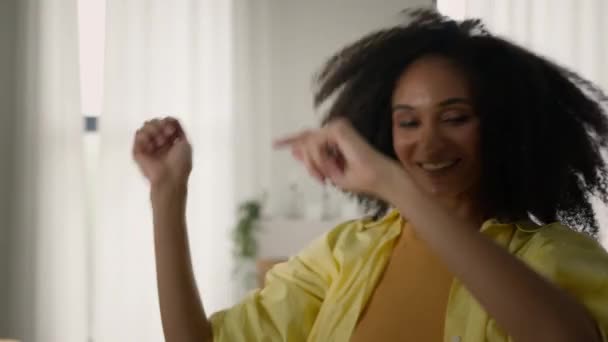 アフリカ系アメリカ人幸せな女性少女 リビングルームでカーリーヘアと楽しいダンスアクティブモーションジャンプ無料週末を祝うホーム面白いパーティーでダンスを勝ち取る音楽移転移動 — ストック動画
