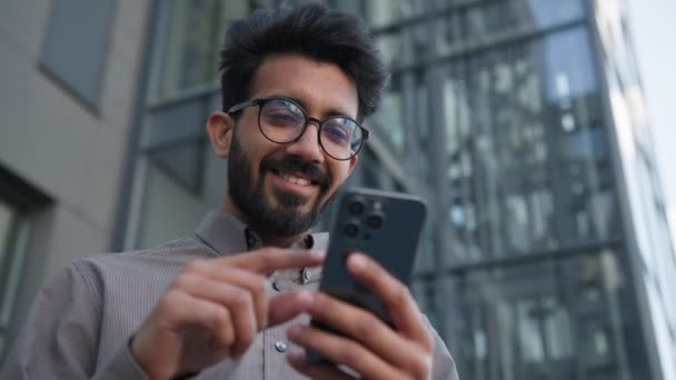 ハッピー驚いた男インドアラビアのビジネスマンは屋外で携帯電話のガジェットを使用して驚くべきニュースを受け取ります 男性雇用主 ラッキー勝者 オンラインベットビジネスの達成 Euphoria 都市での勝利を喜びます — ストック動画