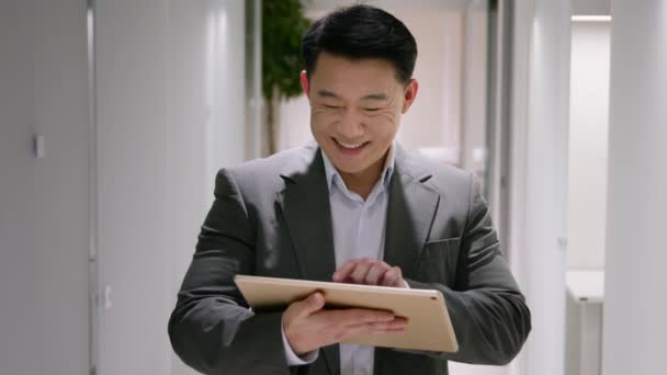 快乐的亚洲中年男人中国韩国商人笑容满面的企业雇主在办公室走廊使用数字平板电脑游说男性企业家在便携式设备上浏览互联网社交媒体 — 图库视频影像
