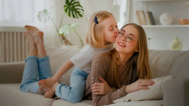Mutlu annelik bağı kuran sevgi dolu beyaz anne kanepeye uzanmış küçük kız çocuğu sırtımda anne öpücükleri sevimli ebeveyn sıcak iletişimi tatlı şefkat