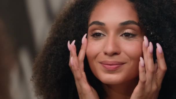 クリームを塗る美しい顔に触れる若いアフリカ系アメリカ人女性はミラー完璧なスキンケア自然な美しさの健康なきれいな保湿された柔らかい保湿された栄養価の高い顔の化粧品で構成します — ストック動画
