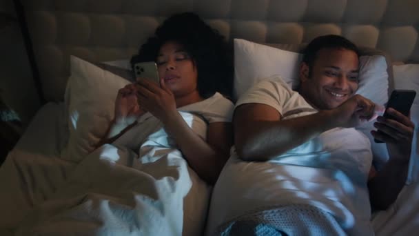 非洲裔美国人夫妇家庭女人们女朋友男友的妻子丈夫在黑暗床的卧室里晚上翻动智能手机浏览手机社交媒体工具成瘾 — 图库视频影像
