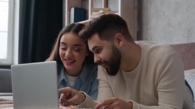 Beyaz bir çift, ev sahibi gülümseyen kadın ve koca dizüstü bilgisayar kullanıyor. Yatakta birlikte rahatlayın. İnternette sörf yapan internet sitesi.