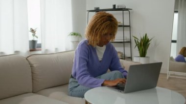 Afro-Amerikalı kadın kullanıcı serbest çalışan iş kadını ev oturma odasında internetten öğrenim görüyor dizüstü bilgisayarını bitiriyor bilgisayar alışverişini başarıyor kanepeye rahatça gülümsüyor.