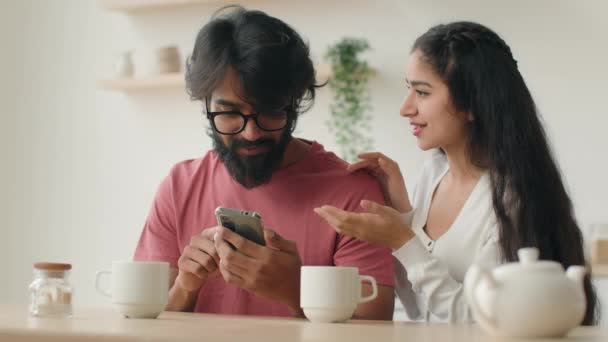 アラビアのインドのカップル女性ガールフレンドと男のボーイフレンドの話 携帯電話を使用して オンライン注文は アパートのインターネットショッピング配信のための商品を選択します 笑顔の多民族家族現代ガジェット中毒 — ストック動画